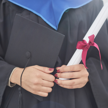 A woman in a graduation gown, holding her graduation cap and diploma